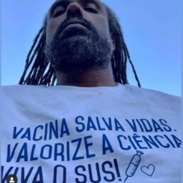#Audiodescrição: Homem negro de dreads pretos longos e barba. Usa camisa branca escrito: Vacina salva vidas. Valorize a ciência. Viva o SUS!