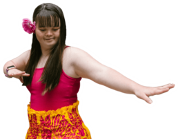 #Audiodescrição: Mulher branca com Síndrome de Down. Ela tem cabelo longo castanho e uma flor rosa na orelha, usa camiseta rosa e saia amarela com desenhos de folhas de plantas rosa.