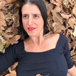 #Audiodescrição: Mulher branca de cabelo preto na altura dos ombros, usa camisa preta e está deitada entre folhas secas.